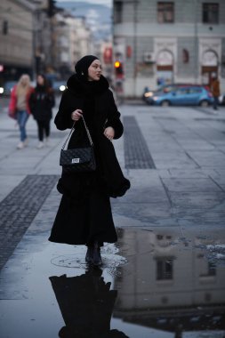 Soğuk bir kış gecesinde şehir caddesinde yürüyen Müslüman bir kadın arka planda Bokeh şehir ışıklarıyla tesettüre girmiş.