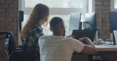 Afro-Amerikan iş adamı ve turuncu saçlı modern bir iş kadını, bilgisayar kullanarak çağdaş ofis ortamında iş sorunlarını çözümlemek için işbirliği yapıyorlar.