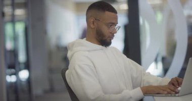 Modern ofis ortamında, Afrikalı Amerikalı bir işadamı özenle dizüstü bilgisayarı üzerinde çalışıyor, profesyonel çevresindeki kararlılığı, hırsı ve verimliliği somutlaştırıyor.. 