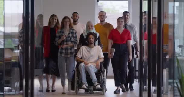 一群形形色色的年轻人聚集在一个玻璃封闭的现代创业办公室里 与坐在轮椅上的一个人 一个非洲裔美国年轻人和一个头巾都是包容性的 — 图库视频影像