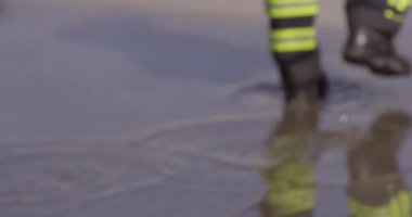 Bir itfaiyecinin kararlı adımlarını yakına çekerek itfaiye aracına doğru yürürken sarsılmaz bir adanmışlıkla acil bir duruma müdahale etmeye hazır olduğunu gösterir.. 