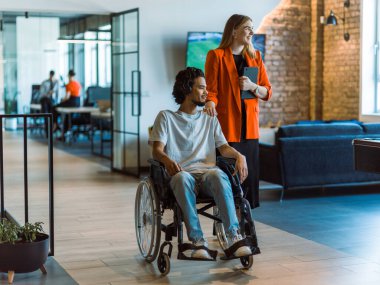 Tekerlekli sandalyedeki Afro-Amerikalı işadamı, iş arkadaşı ile tablet kullanarak uyumlu teknolojinin kusursuz bütünleşmesini ve