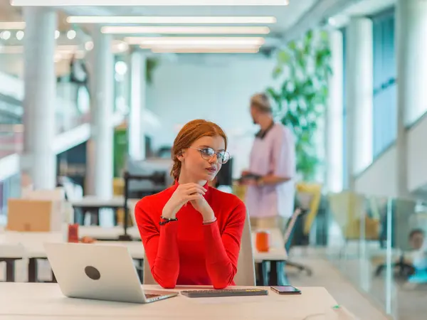 In a modern startup office, a professional businesswoman with orange hair sitting at her laptop, epitomizing innovation and productivity in her contemporary workspace.