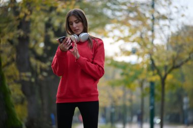 Sportif kadın egzersiz yapmadan önce akıllı telefonu kontrol eder. Kırmızı giyinmiş kablosuz kulaklıkla müzik dinler.