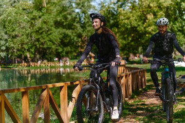 Profesyonel bisiklet kıyafetleriyle süslenmiş mutlu bir çift, parkın içinde romantik bir bisiklet sürmekten hoşlanıyor, modern doğal cazibelerle çevrili, sevgi ve mutluluk saçıyor.. 