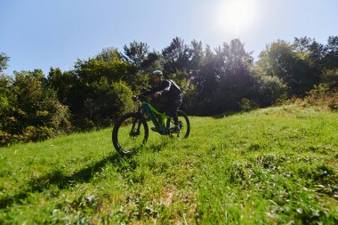  Güneşli bir günün ışıltısında, spor kıyafetlerini giymiş spor meraklısı bisikletiyle parkta pedal çeviriyor, dinamik bir açık hava sporunda kuvvet ve canlılık simgeliyor.. 