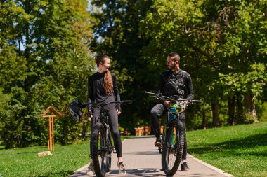 Bisikletlerle donatılmış ve yolculuklarını koordine etmeye odaklanmış tatlı bir çift, parkta manzaralı rotalar planlarken GPS mobil ve saatlerini kontrol ediyor, kusursuz bir şekilde harmanlama teknolojisi ve