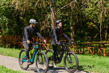 Profesyonel bisiklet kıyafetleriyle süslenmiş mutlu bir çift, parkın içinde romantik bir bisiklet sürmekten hoşlanıyor, modern doğal cazibelerle çevrili, sevgi ve mutluluk saçıyor.. 