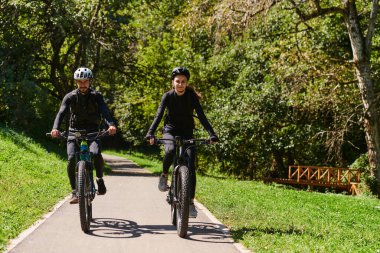 Profesyonel bisiklet kıyafetleriyle süslenmiş mutlu bir çift, parkın içinde romantik bir bisiklet sürmekten hoşlanıyor, modern doğal cazibelerle çevrili, sevgi ve mutluluk saçıyor.. 