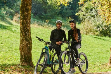 Bisikletlerle donatılmış ve yolculuklarını koordine etmeye odaklanmış tatlı bir çift, parkta manzaralı rotalar planlarken GPS mobil ve saatlerini kontrol ediyor, kusursuz bir şekilde harmanlama teknolojisi ve