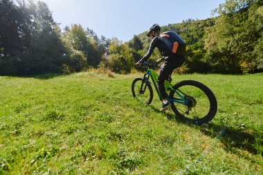 Güneşli bir günün ışıltısında, spor kıyafetlerini giymiş spor meraklısı bisikletiyle parkta pedal çeviriyor, dinamik bir açık hava sporunda kuvvet ve canlılık simgeliyor.. 