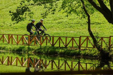 Profesyonel bisiklet kıyafetleriyle süslenmiş mutlu bir çift, parkın içinde romantik bir bisiklet sürmekten hoşlanıyor, modern doğal cazibelerle çevrili, sevgi ve mutluluk saçıyor.. 