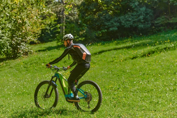 In the radiant glow of a sunny day, a fitness enthusiast, donned in professional gear, pedals through the park on his bicycle, embodying strength and vitality in a dynamic outdoor workout.