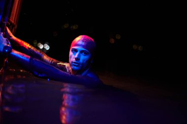 Gerçek bir triatlet yüzücüsüdür. Gölde, neon renkli ışıklarda sıkı bir antrenman sırasında mola verir.
