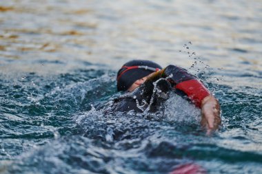 Güneşin doğuşunda gölde yüzen triatlon sporcusu. Dalgıç kıyafeti giymiş. Yüksek kalite fotoğraf