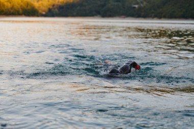 Güneşin doğuşunda gölde yüzen triatlon sporcusu. Dalgıç kıyafeti giymiş. Yüksek kalite fotoğraf