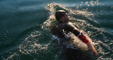 Güneşin doğuşunda gölde yüzen triatlon sporcusu. Dalgıç kıyafeti giymiş. Yüksek kalite fotoğraf