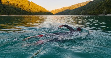 Güneşin doğuşunda gölde yüzen triatlon sporcusu. Dalgıç kıyafeti giymiş. Yüksek kalite fotoğraf