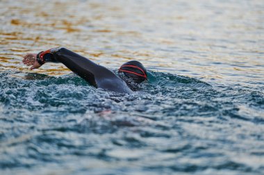 Güneşin doğuşunda gölde yüzen triatlon sporcusu. Dalgıç kıyafeti giymiş. Yüksek kalite fotoğraf