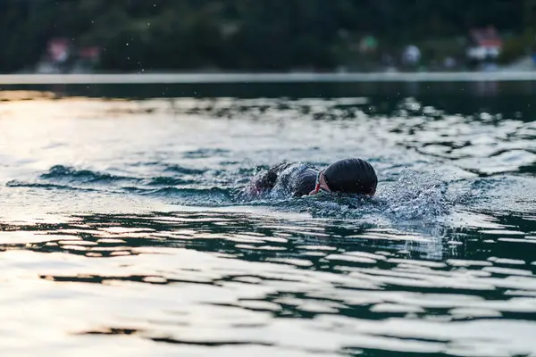 Güneşin doğuşunda gölde yüzen triatlon sporcusu. Dalgıç kıyafeti giymiş. Yüksek kalite fotoğraf