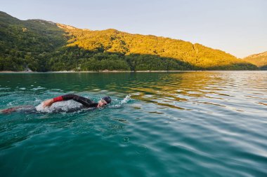 Güneşin doğuşunda gölde yüzen triatlon sporcusu. Dalgıç kıyafeti giymiş. Yüksek kalite fotoğraf