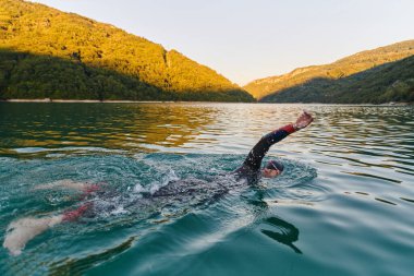 Güneşin doğuşunda gölde yüzen triatlon sporcusu. Dalgıç kıyafeti giymiş. Yüksek kalite fotoğraf