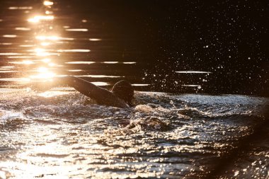 Güneşin doğuşunda gölde yüzen triatlon sporcusu. Dalgıç kıyafeti giymiş. Yüksek kalite fotoğraf