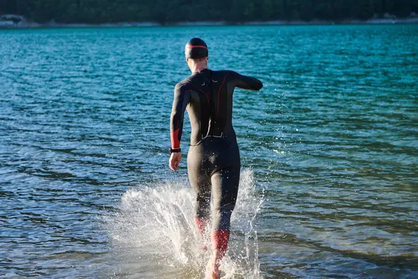 Triathlon athlete starting swimming training on lake.