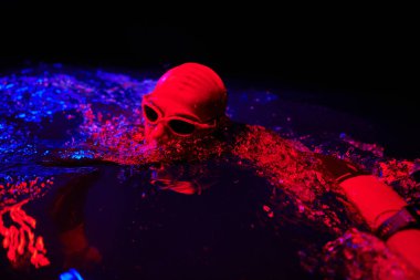 Gerçek bir triatlet yüzücüsüdür. Gölde, neon renkli ışıklarda sıkı bir antrenman sırasında mola verir.