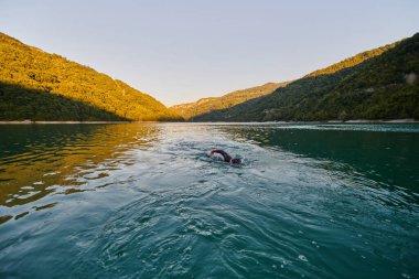 Güneşin doğuşunda gölde yüzen triatlon sporcusu. Dalgıç kıyafeti giymiş. Yüksek kalite fotoğraf