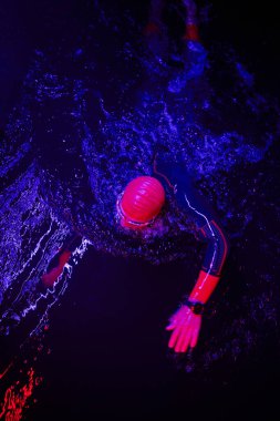 Gerçek bir triatlet yüzücüsüdür. Gölde, neon renkli ışıklarda sıkı bir antrenman sırasında mola verir.