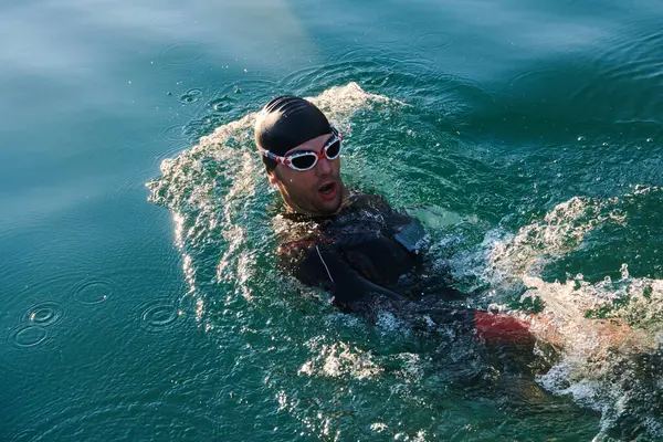Triathlon athlete swimming on lake in sunrise wearing wetsuit. High quality photo