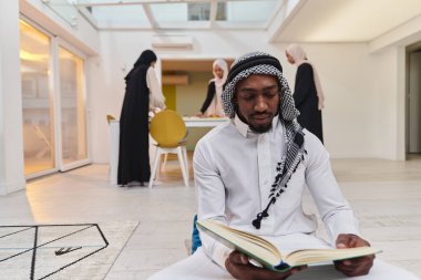 Kutsal Ramazan ayında, Kuran okumaya dalmış Afrikalı bir Müslüman adam üç tesettürlü kadının iftar için yemek hazırlayıp servis ettiği bir zemin ile çevrilidir.