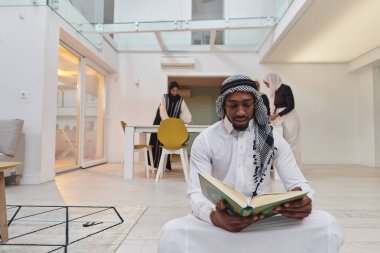 Kutsal Ramazan ayında, Kuran okumaya dalmış Afrikalı bir Müslüman adam üç tesettürlü kadının iftar için yemek hazırlayıp servis ettiği bir zemin ile çevrilidir.