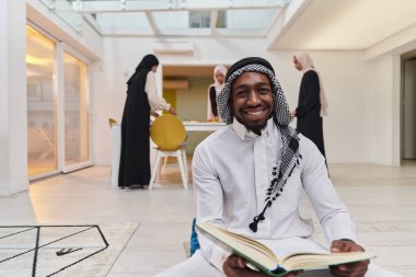Kutsal Ramazan ayında, Kuran okumaya dalmış Afrikalı bir Müslüman adam üç tesettürlü kadının iftar için yemek hazırlayıp servis ettiği bir zemin ile çevrilidir.