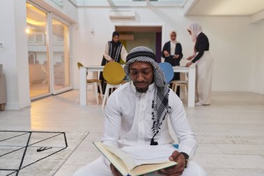 Kutsal Ramazan ayında, Kuran okumaya dalmış Afrikalı bir Müslüman adam üç tesettürlü kadının iftar için yemek hazırlayıp servis ettiği bir zemin ile çevrilidir.
