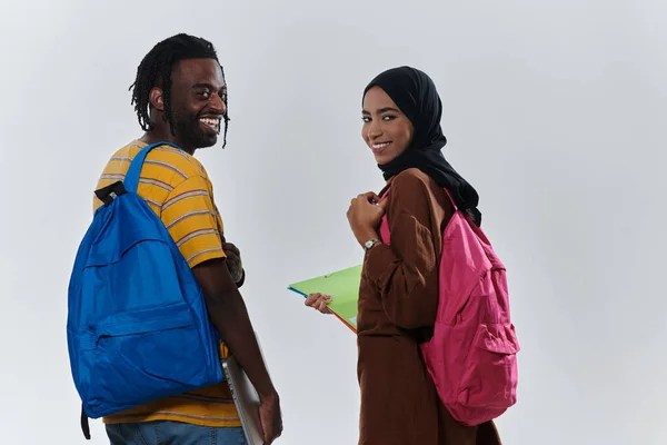 African American student collaborates with his Muslim colleague, who diligently works on her laptop, symbolizing a blend of diversity, modern learning, and cooperative spirit against a serene white