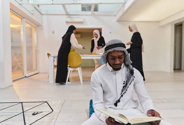 Kutsal Ramazan ayında, Kuran okumaya dalmış Afrikalı bir Müslüman adam üç tesettürlü kadının iftar için yemek hazırlayıp servis ettiği bir zemin ile çevrilidir.