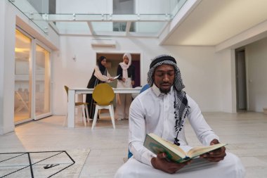 Kutsal Ramazan ayında, Kuran okumaya dalmış Afrikalı bir Müslüman adam üç tesettürlü kadının iftar için yemek hazırlayıp servis ettiği bir zemin ile çevrilidir.