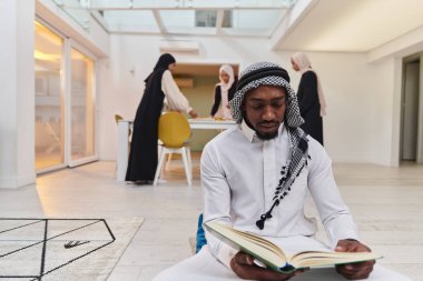 Kutsal Ramazan ayında, Kuran okumaya dalmış Afrikalı bir Müslüman adam üç tesettürlü kadının iftar için yemek hazırlayıp servis ettiği bir zemin ile çevrilidir.