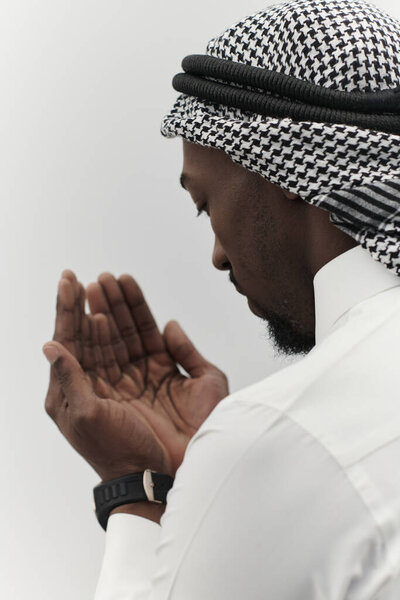 African American Muslim man raises his hands in prayer, seeking solace and devotion to God, as he stands isolated against a serene white backdrop, symbolizing a profound expression of faith and