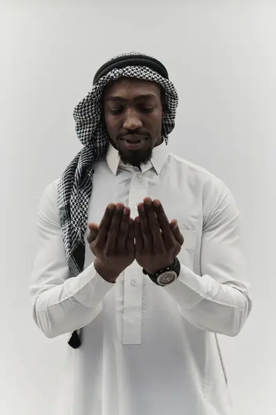 アフリカ系アメリカ人のムスリム男性は祈りの中で手を挙げ 神に平和と献身を求め 穏やかな白い背景に孤立し 深い信仰の表現を象徴しています — ストック写真