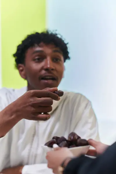 African American Muslim man delicately takes dates to break his fast during the Ramadan month, seated at the family dinner table, embodying a scene of spiritual reflection, cultural tradition, and the