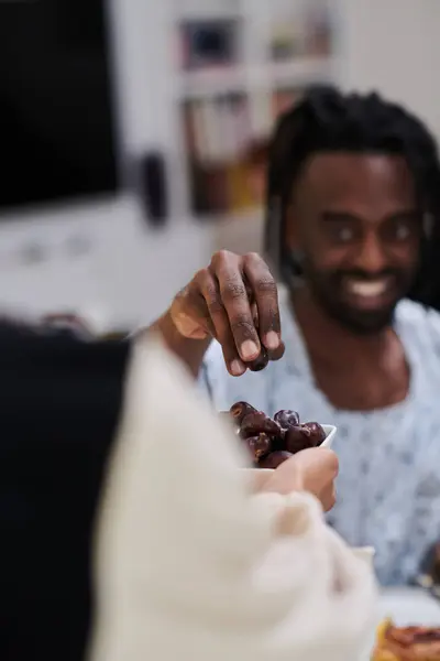 African American Muslim man delicately takes dates to break his fast during the Ramadan month, seated at the family dinner table, embodying a scene of spiritual reflection, cultural tradition, and the