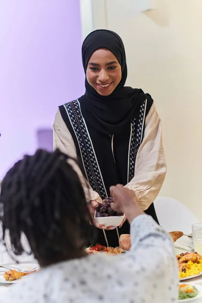 In a heartwarming scene during the sacred month of Ramadan, a traditional Muslim woman offers dates to her family gathered around the table, exemplifying the spirit of unity, generosity, and cultural