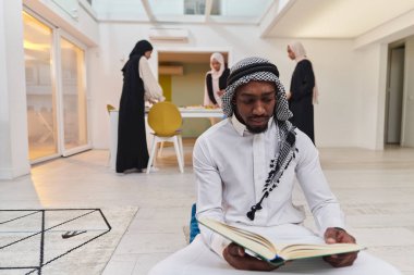 Kutsal Ramazan ayında, Kuran okumaya dalmış Afrikalı bir Müslüman adam üç tesettürlü kadının iftar için yemek hazırlayıp servis ettiği bir zemin ile çevrilidir.