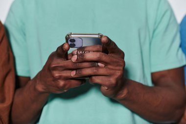 Afro-Amerikalı genç, çağdaş dijital bağlantı ve gençlik kültürünün özünü özetleyen el değmemiş beyaz bir arka plan karşısında akıllı telefonuyla meşgul oluyor.. 