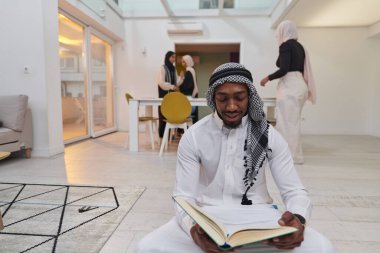Kutsal Ramazan ayında, Kuran okumaya dalmış Afrikalı bir Müslüman adam üç tesettürlü kadının iftar için yemek hazırlayıp servis ettiği bir zemin ile çevrilidir.