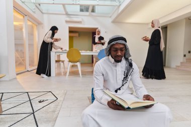 Kutsal Ramazan ayında, Kuran okumaya dalmış Afrikalı bir Müslüman adam üç tesettürlü kadının iftar için yemek hazırlayıp servis ettiği bir zemin ile çevrilidir.