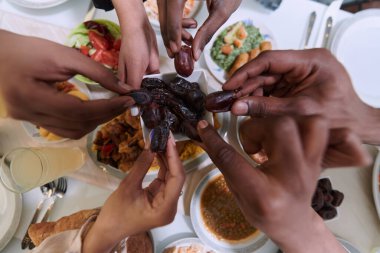 Dokunaklı bir yakın plan çekimde, Müslüman bir ailenin farklı elleri, kutsal Ramazan ayı boyunca orucun kırılışını sembolize ederek, kültürel birliğin bir anını yakalıyor.